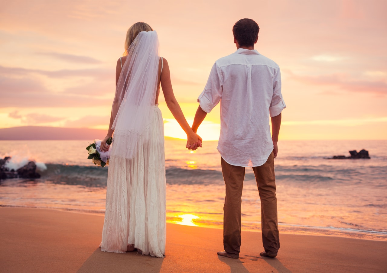 Married couple, bride and groom at sunset on beautiful tropical beach in Hawaii